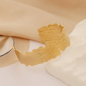 Detailed view of wide hollowed-out hammered texture golden cuff bracelet on silk