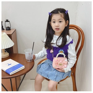 Detail view of pink quilted handbag with pearl handle and cartoon charms on young girl