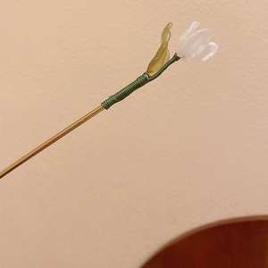 Detail of floral hairpin with translucent white buds and green leaves on gold stick