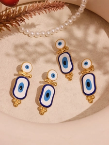 Macro detail of gold evil eye earrings with blue enamel finish on cream textured surface