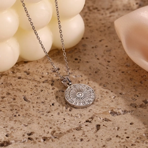 Detailed close-up of a silver compass pendant necklace on textured stone background