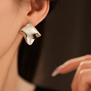Détail d'une boucle d'oreille carrée torsadée argentée au design géométrique minimaliste