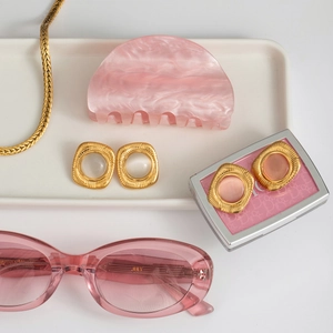 Close-up of ribbed square cat eye earrings with matching pink fashion accessories on tray