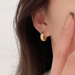 Close-up of gold gear-textured stud earrings worn by a model to show detail and metallic shine