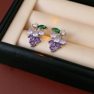 Macro view of purple and green zircon grape earrings on a beige velvet jewelry box liner