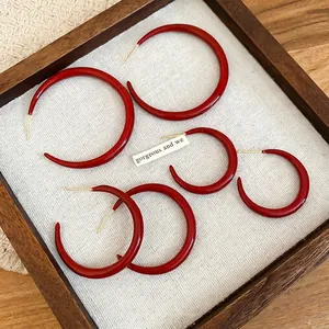 Three pairs of vintage red C-shaped hoop earrings in different sizes on a wooden tray