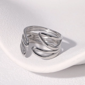 Close-up of a silver multilayer winding stainless steel ring on a white textured surface