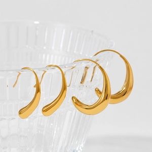 Polished gold C-shaped stainless steel hoop earrings set of four displayed on glassware