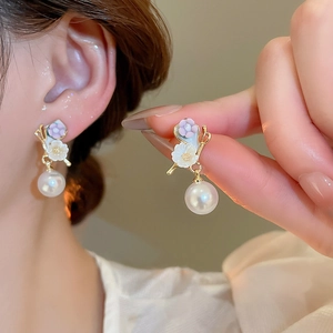 Gros plan de boucles d'oreilles fleuries dorées avec pétales mauves et perle blanche