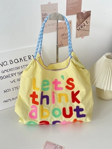 Detail of yellow canvas tote bag with colorful embroidery and blue checkered handles