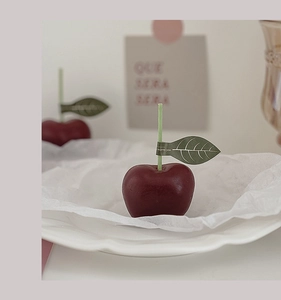 Vista detallada de una vela aromática con forma de cereza roja y hoja en un plato blanco