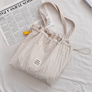 Close-up of pleated beige tote bag with Sozakka label on textured fabric background
