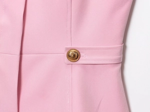 Dettaglio ravvicinato di un bottone dorato a rilievo su tessuto rosa per abiti da donna