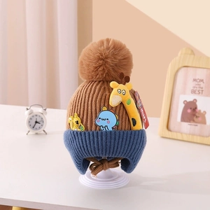 Detail of knitted baby hat with brown pom-pom and cute cartoon giraffe embroidery