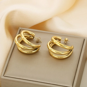 Macro view of gold C-shaped triple-loop earrings on a beige jewelry box with silk