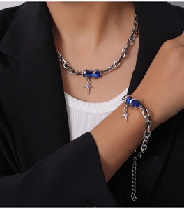 Detail of silver chain necklace and bracelet featuring blue gems and cross pendants