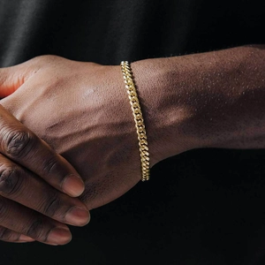 Men's gold plated stainless steel Cuban link bracelet worn on wrist with black background