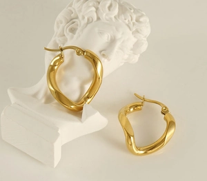 Close-up of golden irregular wave earrings with polished mirror finish on a plaster statue