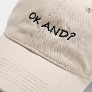 Beige baseball cap with black 'OK AND?' embroidery and cotton twill texture