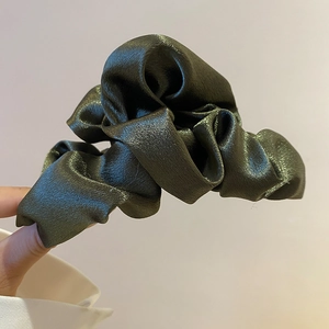 Close-up of dark green pleated satin fabric texture on a cloud-style hair claw clip