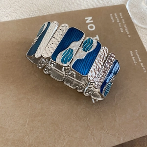 Macro detail of blue enamel square tiles and silver hammered metal texture on elastic bracelet