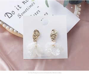 Détail de boucles d'oreilles fleurs dorées avec pétales en nacre sur support