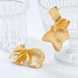 Close-up of gold leaf-shaped earrings with natural petal textures on a clear glass rim