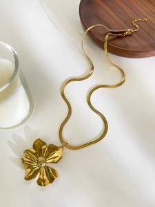 Detail of a large gold floral pendant on a sleek snake chain over a wooden plate