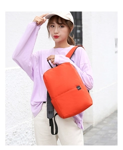 Close-up of lightweight orange backpack worn on shoulder in a bright street setting