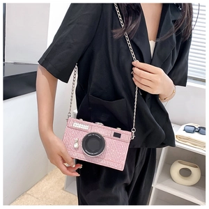 Detail of pink sequin camera-shaped crossbody bag with a silver chain strap worn by a model