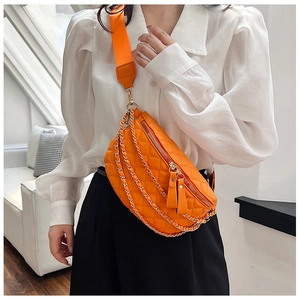Detail of orange quilted waist bag with gold chain and canvas strap on white shirt