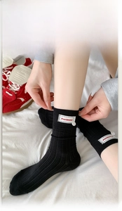 Detail of black ribbed mid-calf socks with white cloth label and decorative button