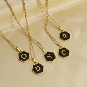 Golden hexagon initial necklaces with black enamel and letters O D Y C R on silk