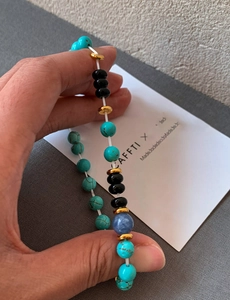 Detailed close-up of turquoise, black agate, and blue gemstone beaded bracelet held by hand