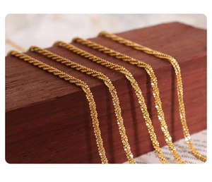 Macro detail of five delicate 18K gold-plated titanium steel anklets on a wooden display