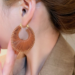 Gros plan d'une grande boucle d'oreille créole tressée marron avec accents dorés
