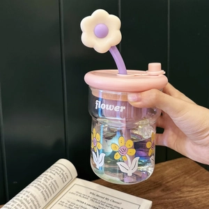 Détail d'une tasse en verre à fleurs avec couvercle rose et paille fleurie violette