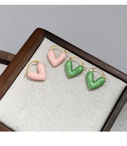 Close-up of pink and green enamel heart earrings with gold hooks on a display tray