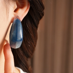 Macro detail of blue teardrop resin earrings with cloudy texture worn on ear