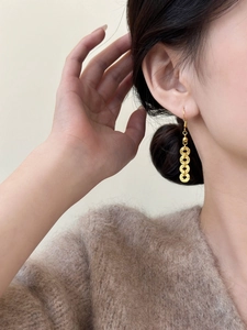Detail of gold-colored round coin tassel earrings worn by model for an elegant retro look