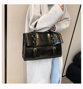 Detail of vintage black leather messenger bag with metal rivets and strap buckles