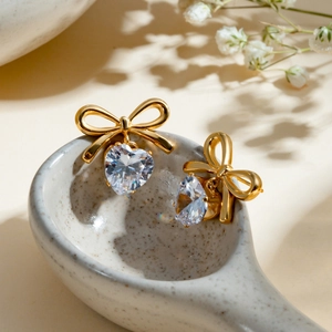 Detailed shot of gold bow earrings with clear heart zircon on a ceramic spoon