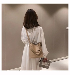 Detail view of khaki leather bucket bag with wide strap and luggage tag decoration