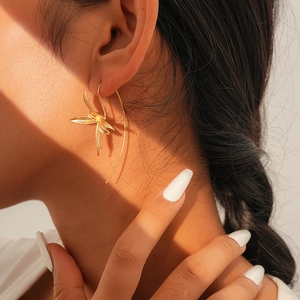 Close-up of golden iris flower earring with curved hook worn by a female model