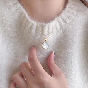 Close-up of golden angel shell pendant on beige sweater with fine gold chain