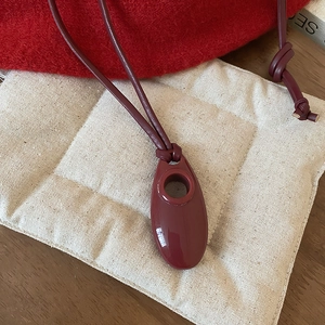 Detail of a deep red oval resin pendant with circular cutout on a slim cord necklace