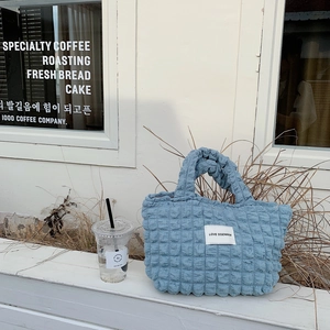Detail of blue bubble textured canvas tote bag featuring a minimalist white woven logo label