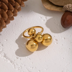 Unique geometric gold ball ring in stainless steel displayed on a rustic stone background