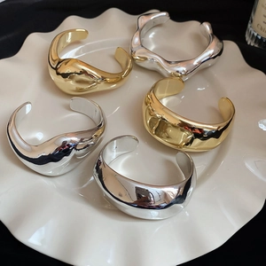 Dettaglio di bracciali geometrici irregolari in oro e argento su un piatto di ceramica