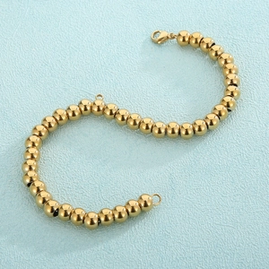 Polished gold stainless steel bead bracelet with lobster clasp on blue leather background